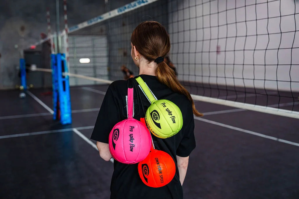 The Pro Spike Flow trio — pink, orange, yellow — resting on Wilson court chairs in a club gym.